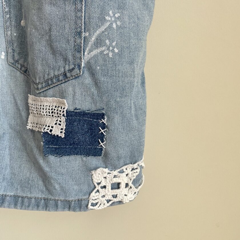 A Patchwork Upcycled Denim Short Romper Overalls with crochet lace on them.