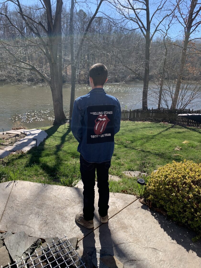 A man standing on a sidewalk wearing a Rolling Stones Upcycled Denim Shirt and looking at the water.
