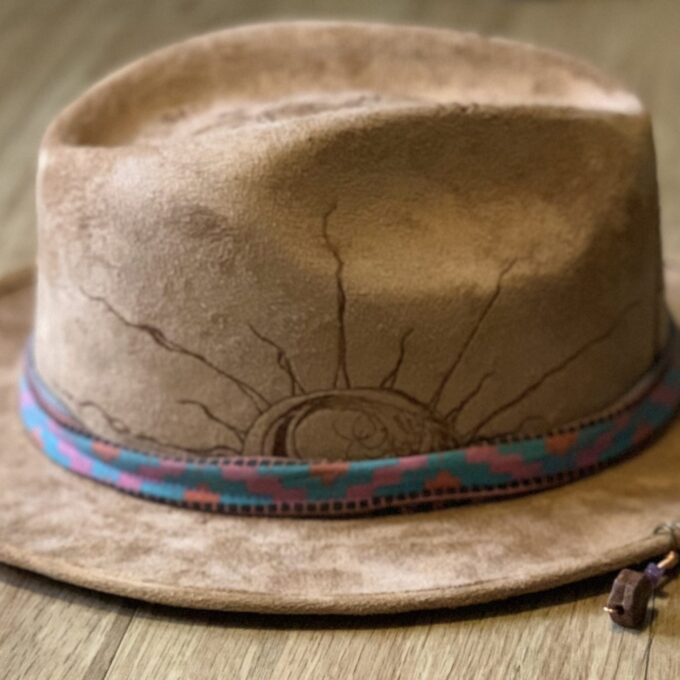 A suede hat wood burned with accessories sitting on top of a wooden table.