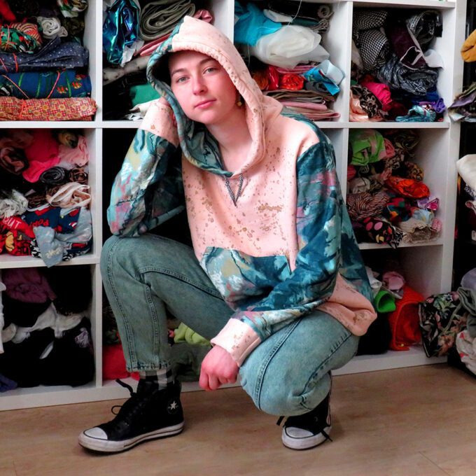 a woman squatting in front of a closet full of Marble-Splatter Hoodies (Medium).