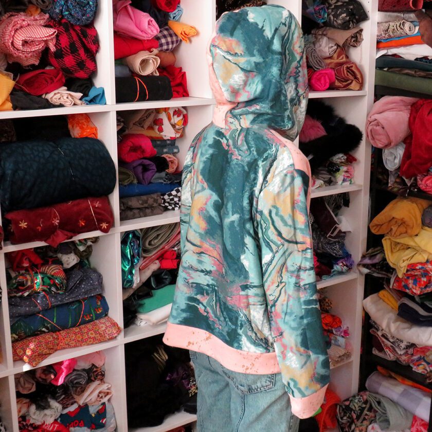 A person standing in front of a closet filled with Marble-Splatter Hoodies (Medium).