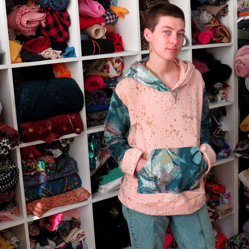 a young boy standing in front of a closet full of Marble-Splatter Hoodies (Medium).