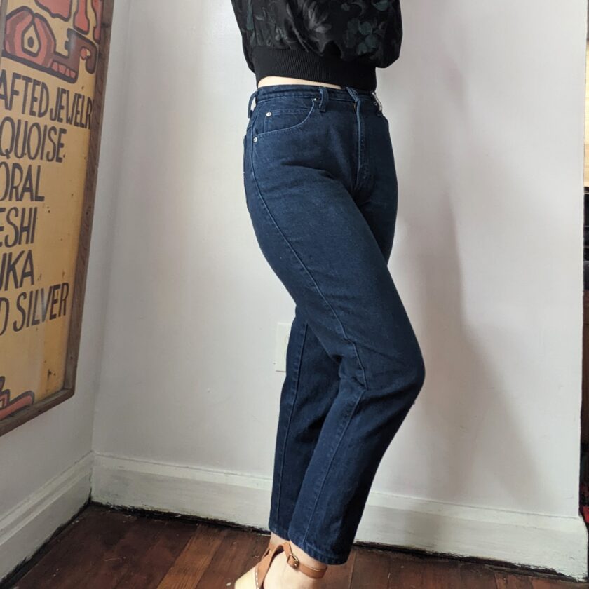 A woman in Reworked Embroidered Rainbow Star Pocket Jeans is leaning against a wall.