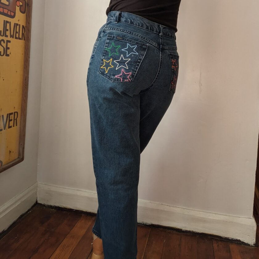 A woman is standing in a room with her back to the camera, wearing Rainbow Star Jeans.