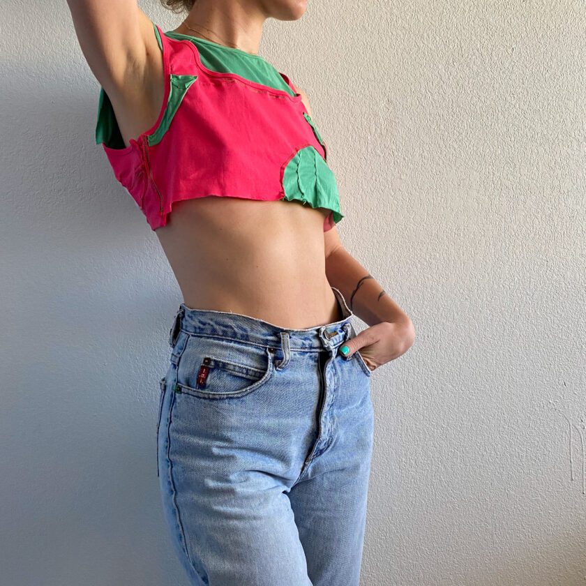 A woman in a 1of1 pink and mint tee tank top leaning against a wall.