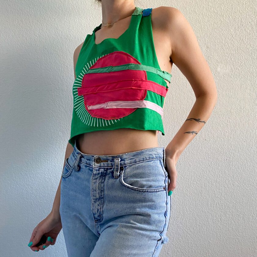 A woman wearing a 1of1 watermelon cross back halter top and jeans.