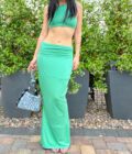 A woman in a 1of1 mint green maxi skirt standing in front of some plants.