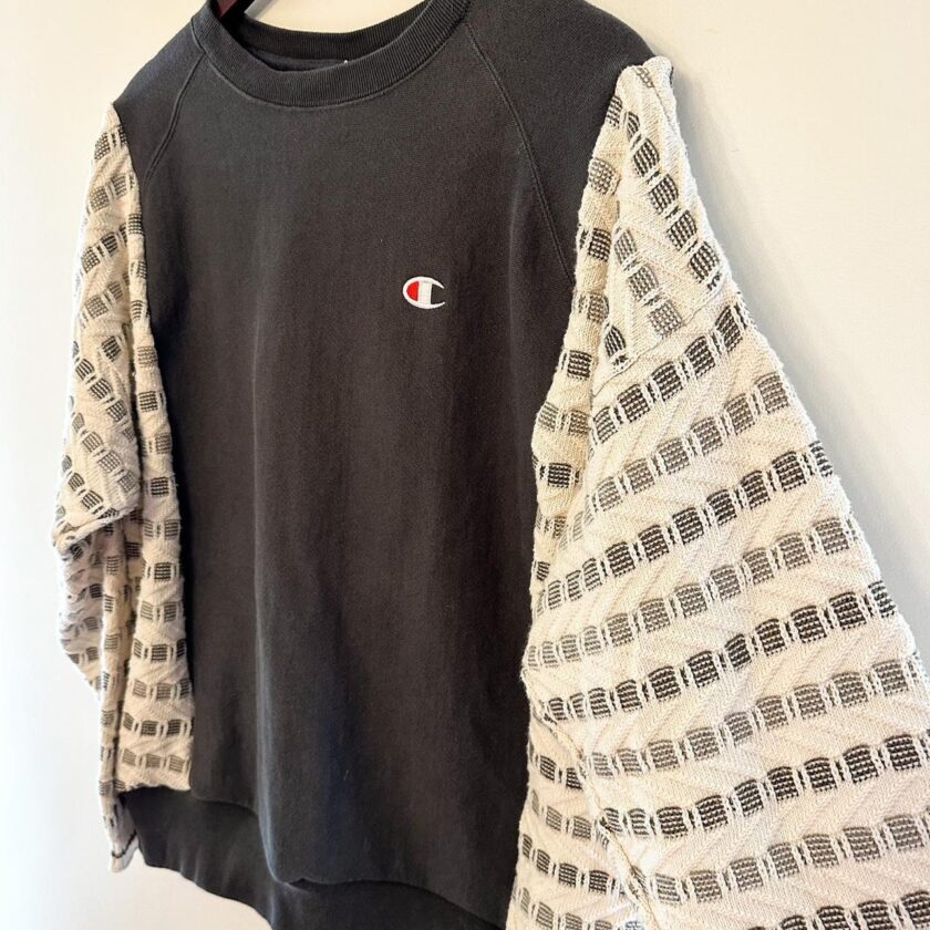 A Reworked Vintage Champion Neutral Crewneck sweater hanging on a wall.