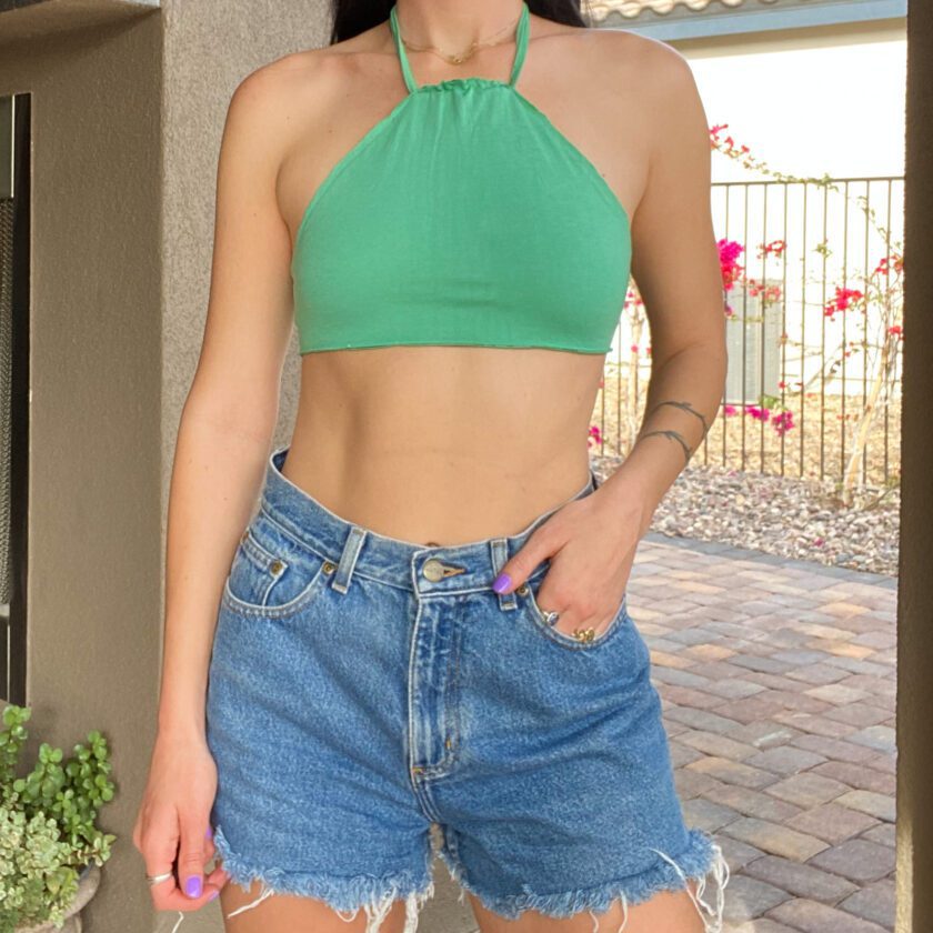 A woman wearing a 1of1 mint green halter top and denim shorts.
