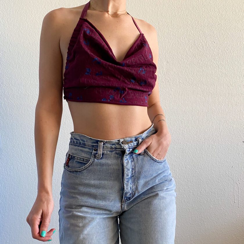 A woman wearing a 1of1 painted text print maroon halter crop top and jeans.