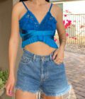 A woman wearing a 1of1 teal blue butterfly halter top and denim shorts.