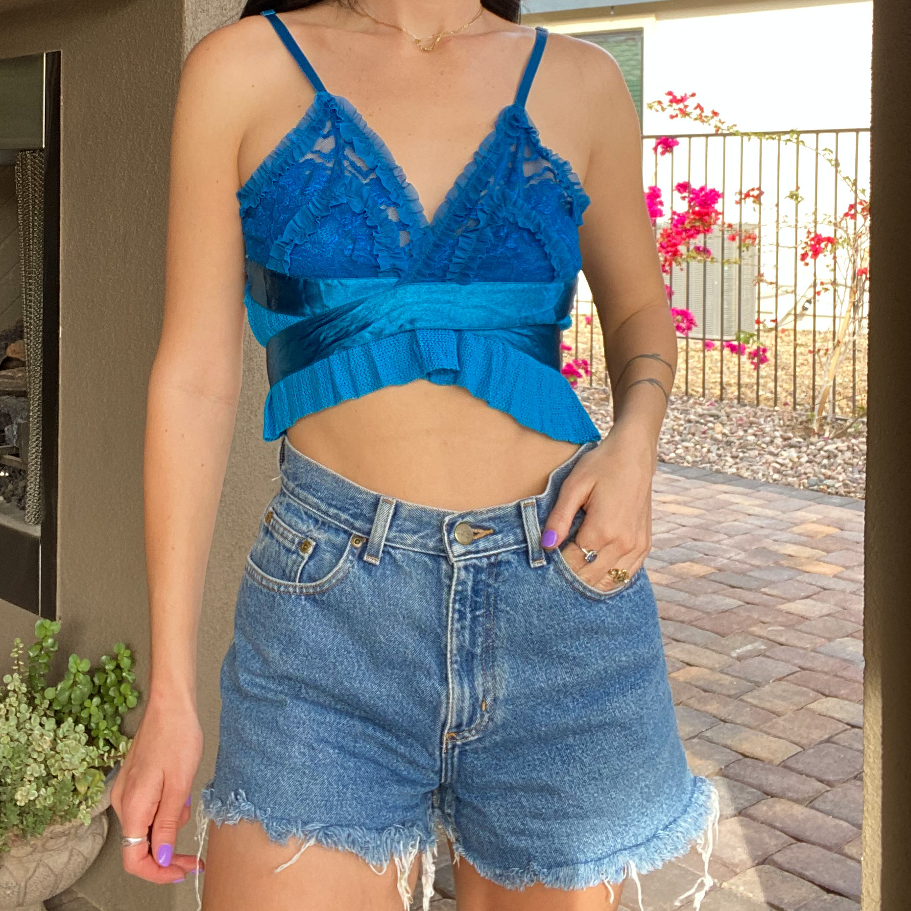 A woman wearing a 1of1 teal blue butterfly halter top and denim shorts.