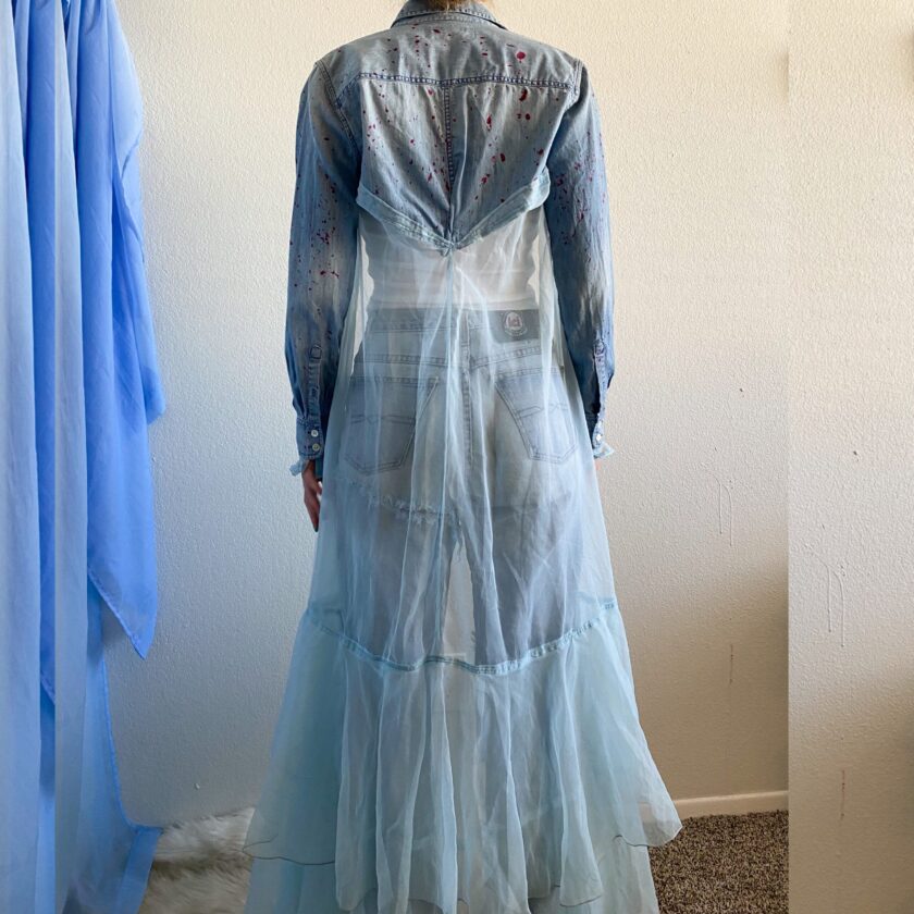 A woman in a 1of1 fairytale feels jacket standing next to a blue curtain.