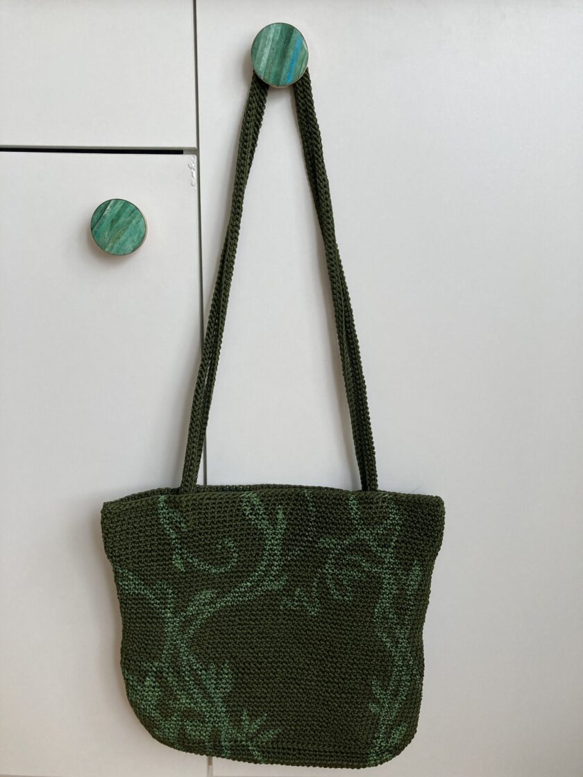 A hand-painted green vines purse hanging on a white wall.