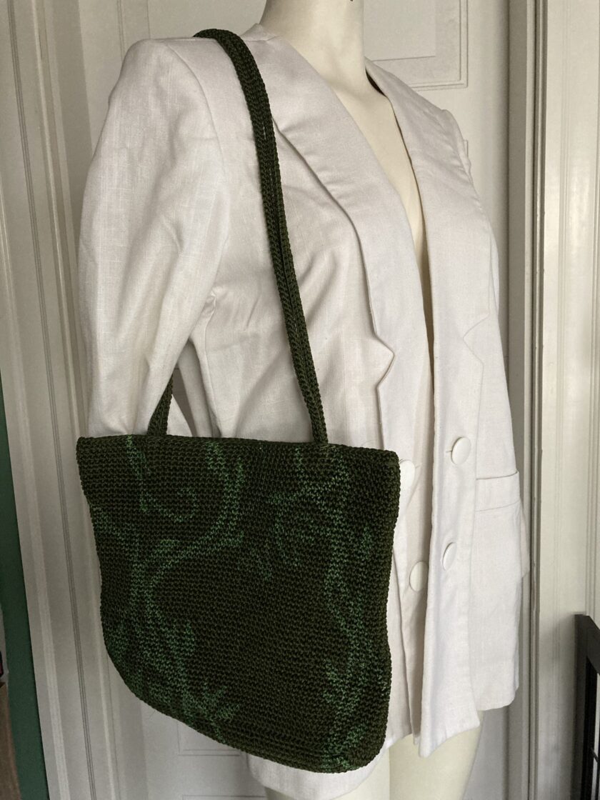 A hand-painted green vines purse sitting on top of a mannequin.