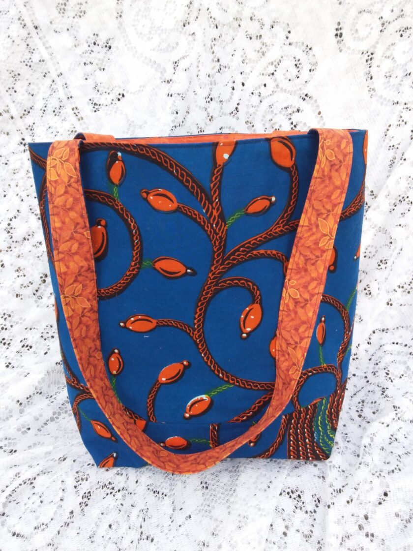 A large market tote handcrafted from vintage blue and orange Tree of Life fabric sits upon a lace background
