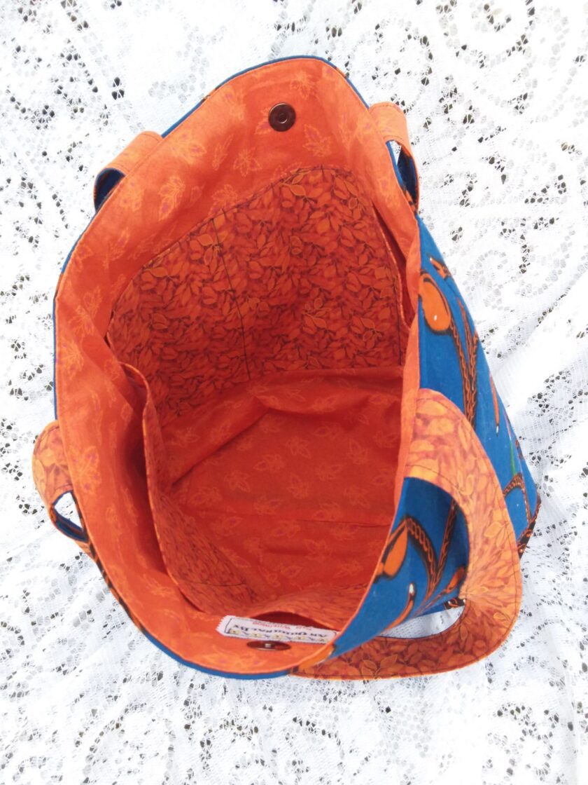Inside this large tote are multiple pockets for keeping goods organized. The bright, orange fabric has a delicate pattern of falling leaves, evoking a fresh autumn feel.
