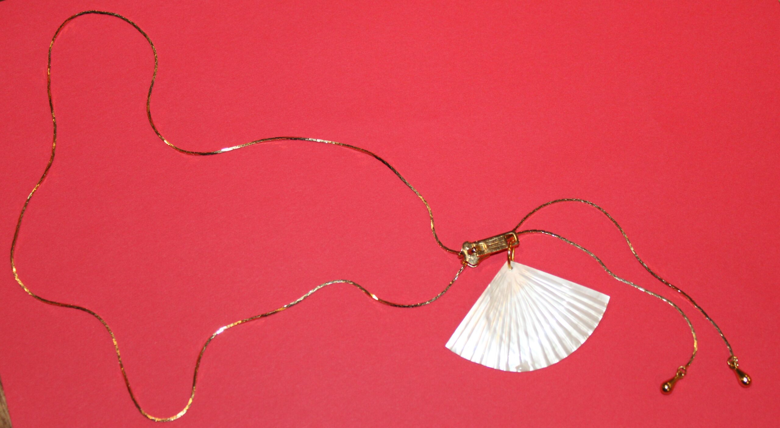 gold tone unique chain with two dangles threaded through a gold zipper and a mother of pearl sculptured fan pendent