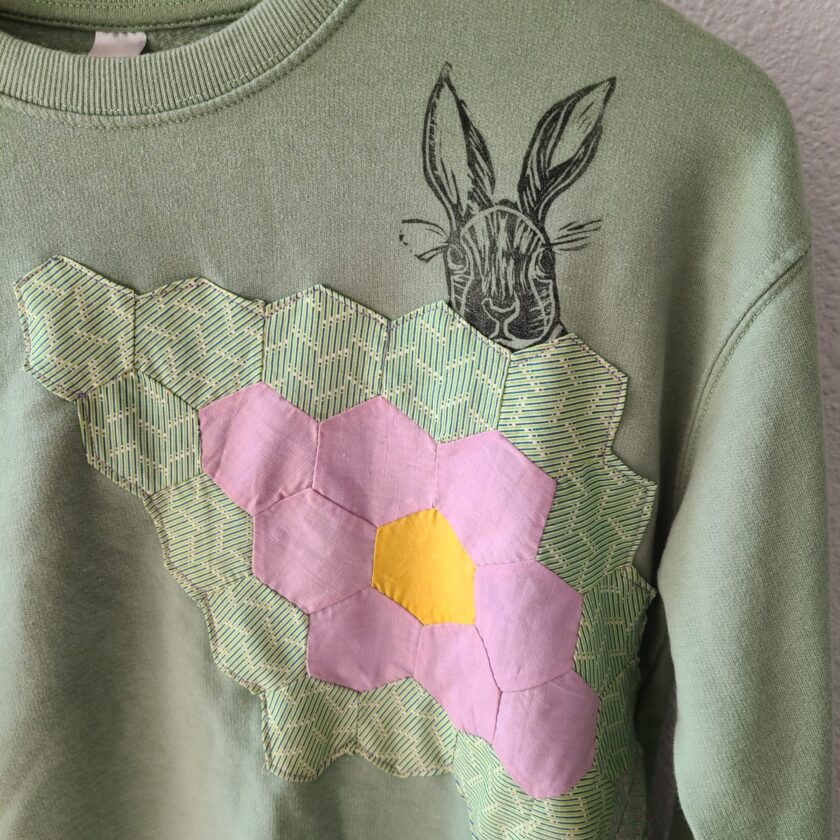 a green sweater with a pink flower on it.