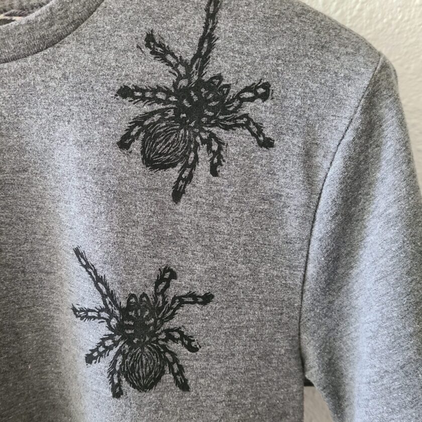 two spiders are embroidered on a grey sweatshirt.
