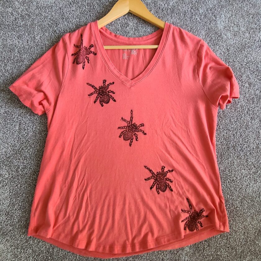 a pink t - shirt with black spiders on it.