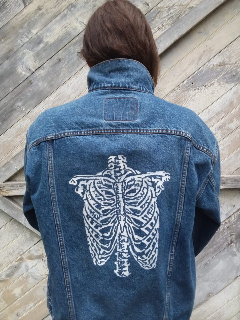 A person wearing an upcycled vintage Levi's jean jacket with a hand painted skeleton on it.