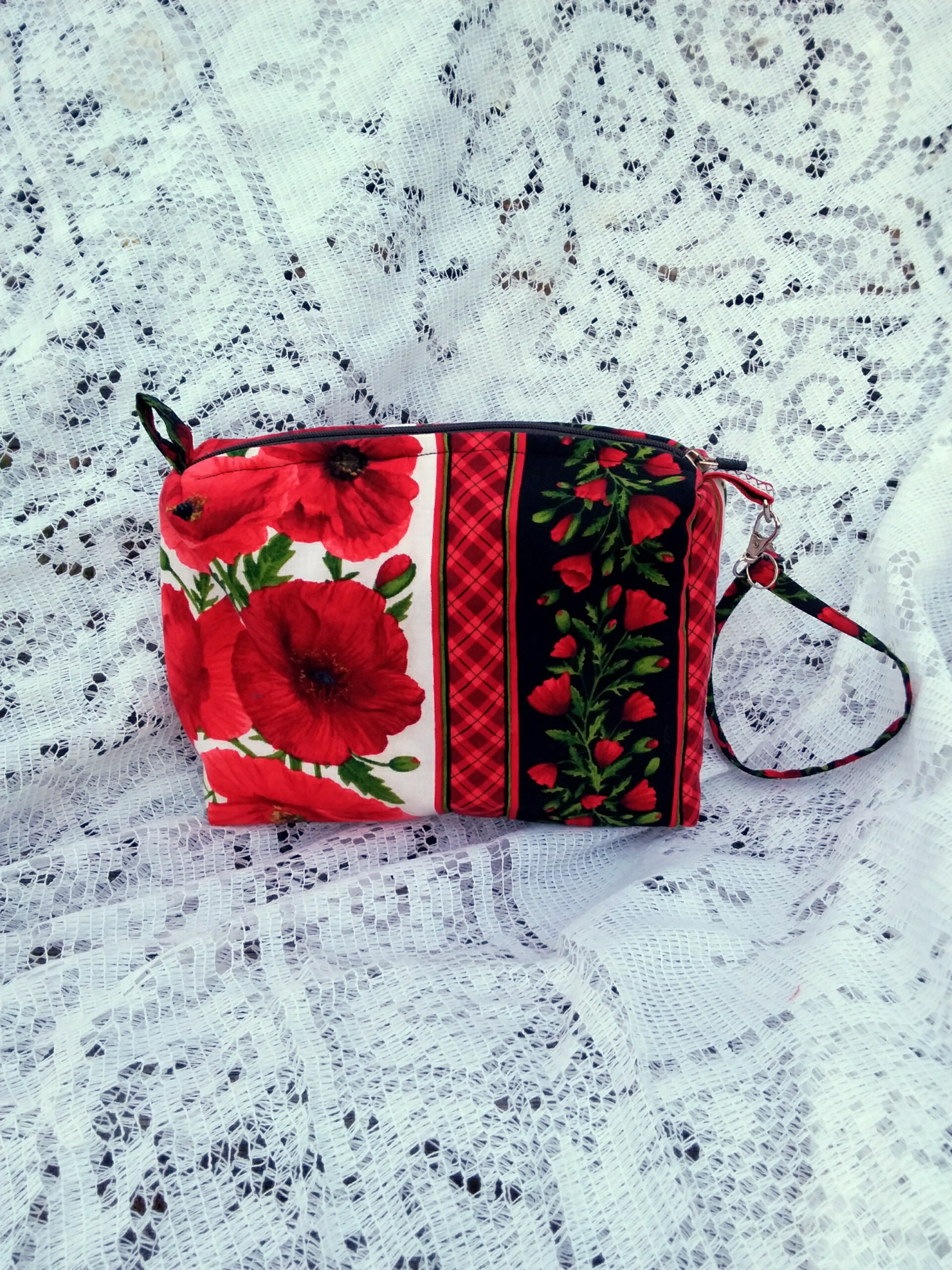 Bold poppy fabric, handcrafted into a quilted wristlet bag rests upon a vintage lace background.