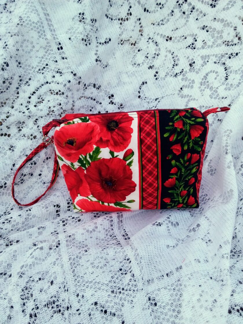 Bold poppy fabric, handcrafted into a quilted wristlet bag rests upon a vintage lace background.