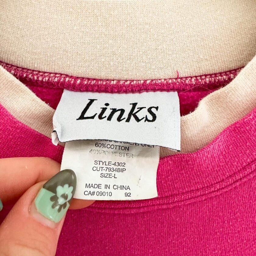 a person is holding a pink sweater with a label on it.