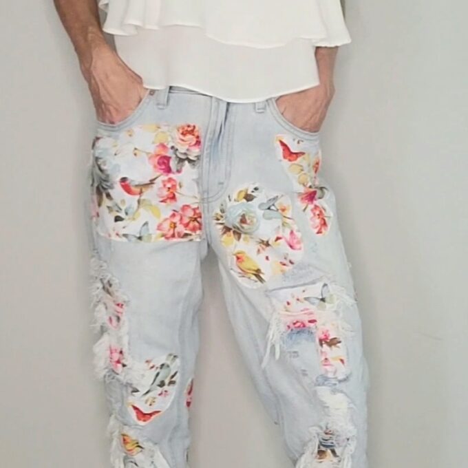 a woman wearing floral ripped jeans and a white tank top.