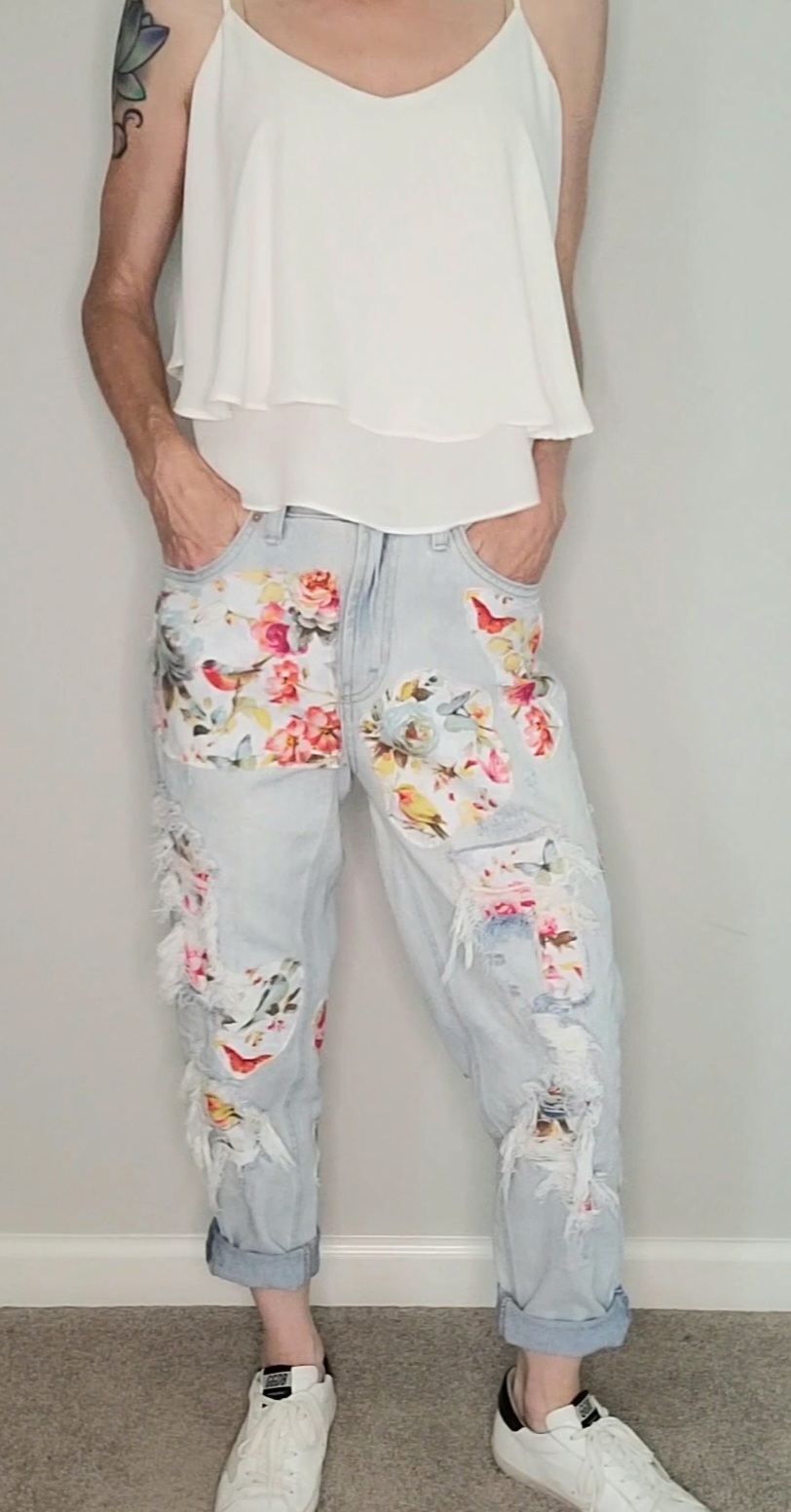 a woman wearing floral ripped jeans and a white tank top.