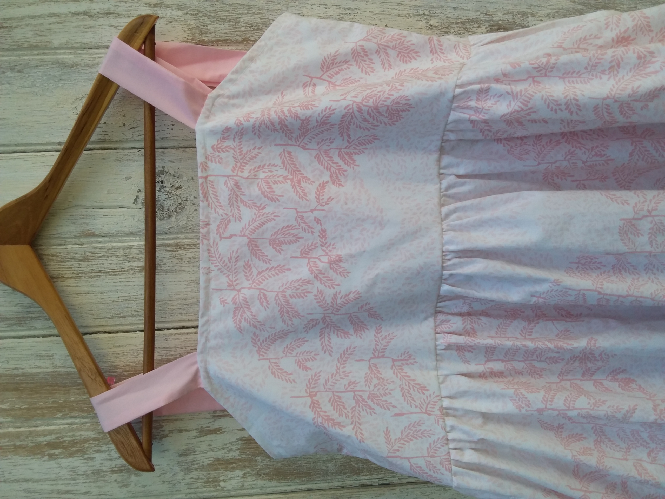 A pink and white dress created from upcycled fabric hanging on a wooden hanger.