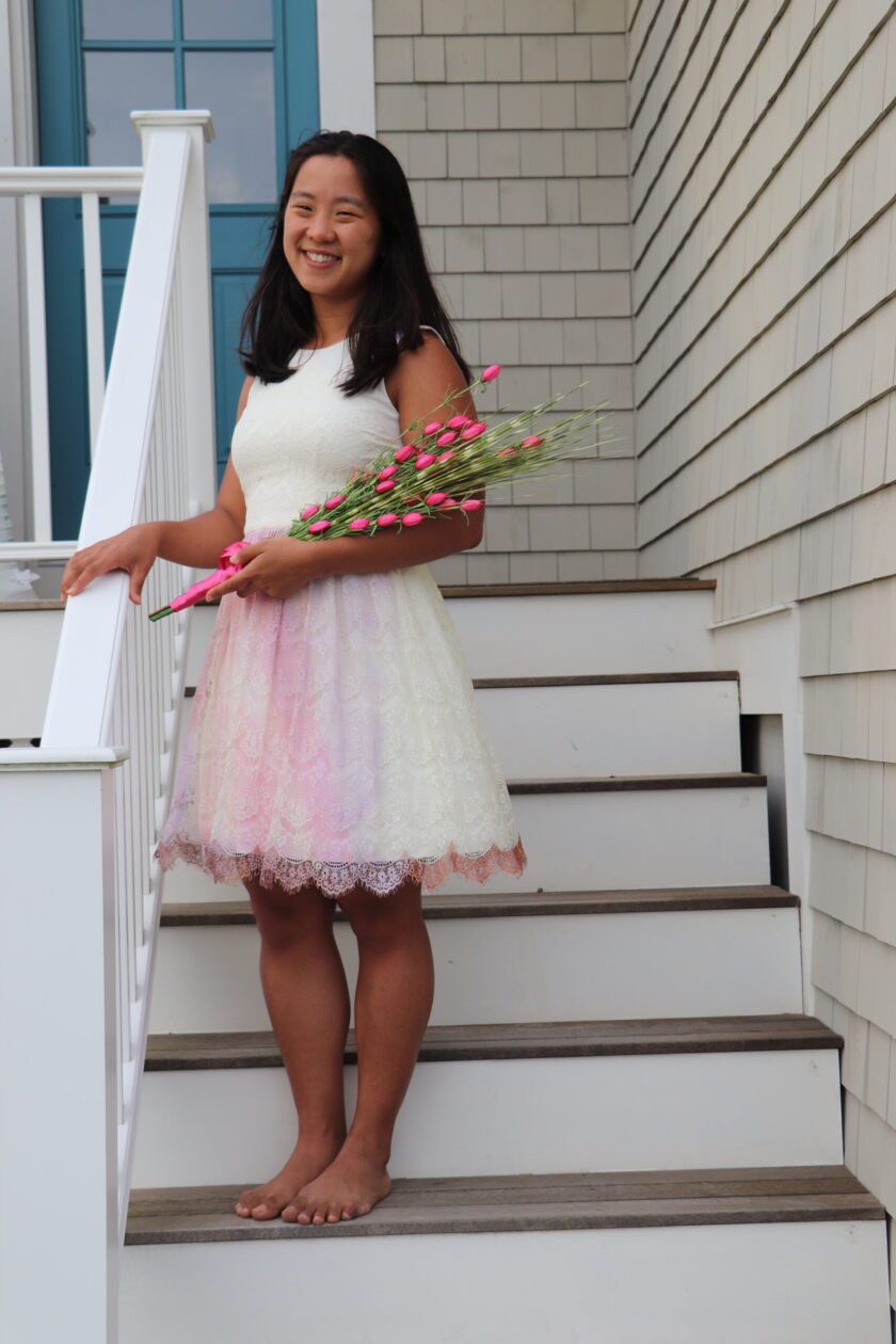 En ung kvinne i en hvit kjole som står på trappen til et hus.