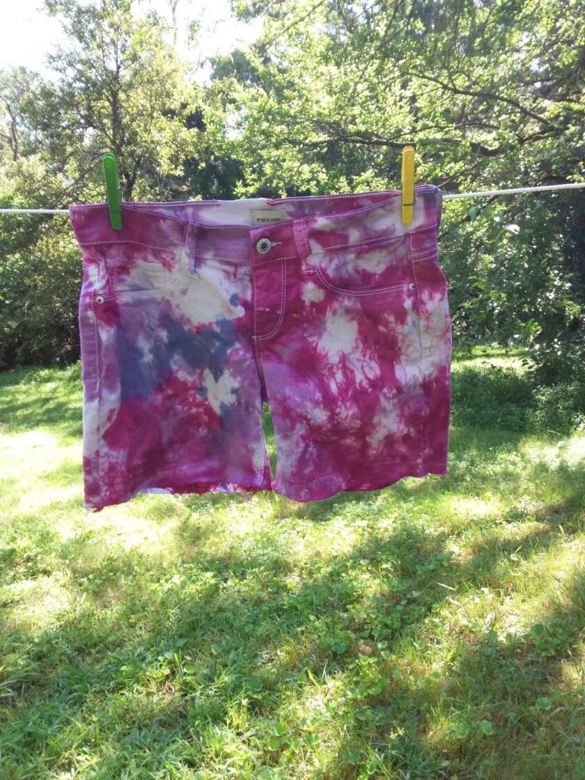 A pair of tie dye shorts hanging on a clothes line.