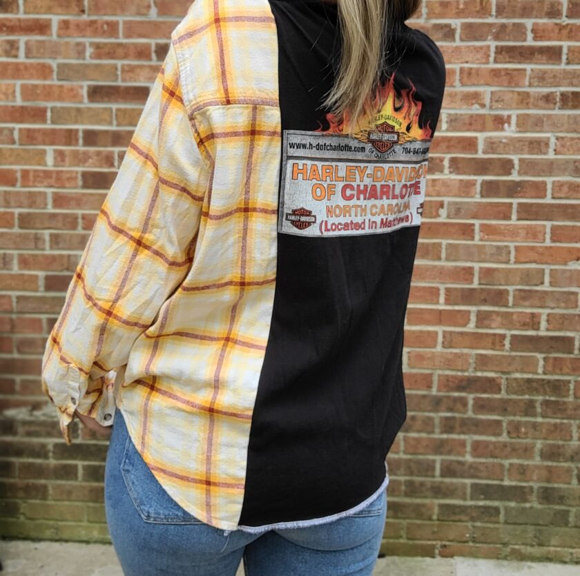 A woman wearing a plaid shirt in front of a brick wall.