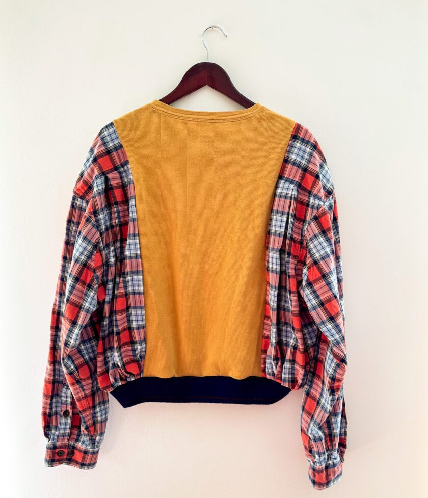 A yellow and blue plaid cropped sweater hanging on a wall.