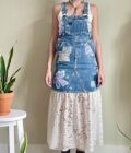 A woman is standing in front of a potted plant wearing a denim overall dress.