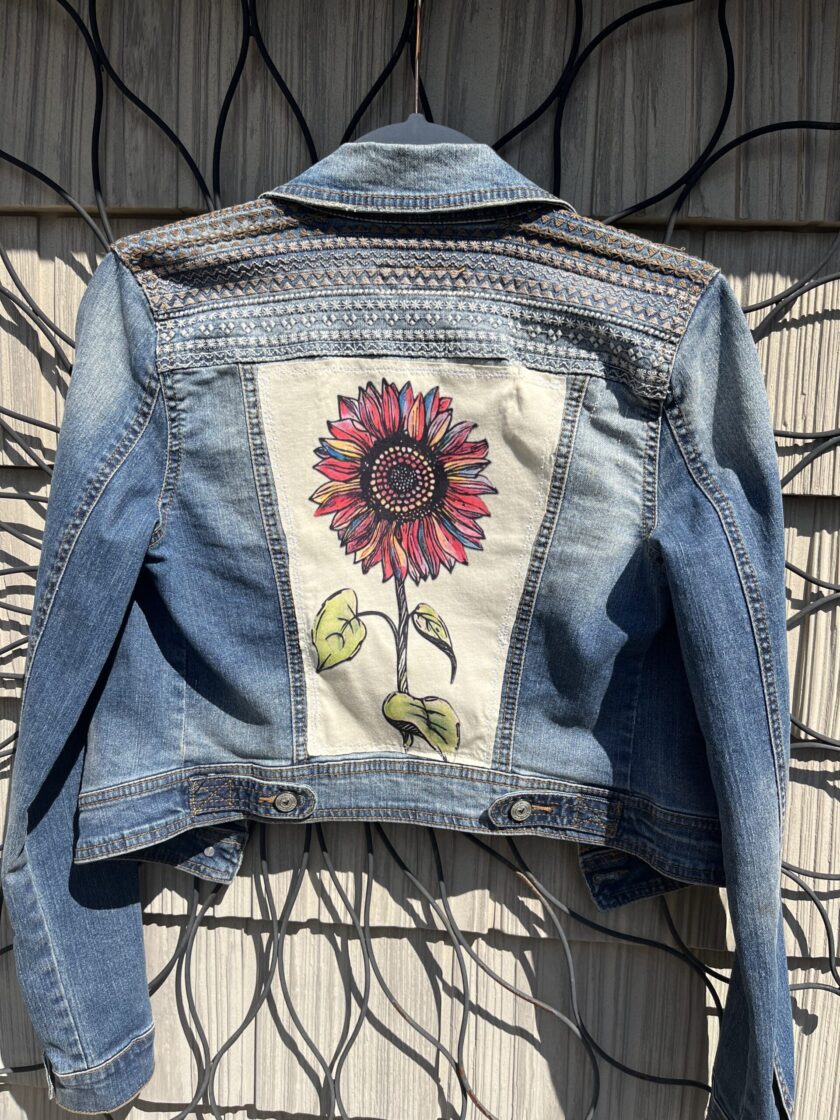 A denim jacket with a sunflower on it.