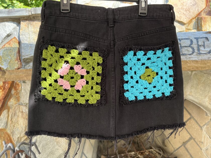 A black denim skirt with crocheted squares on it.
