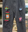 A pair of black jeans with colorful patches on them.