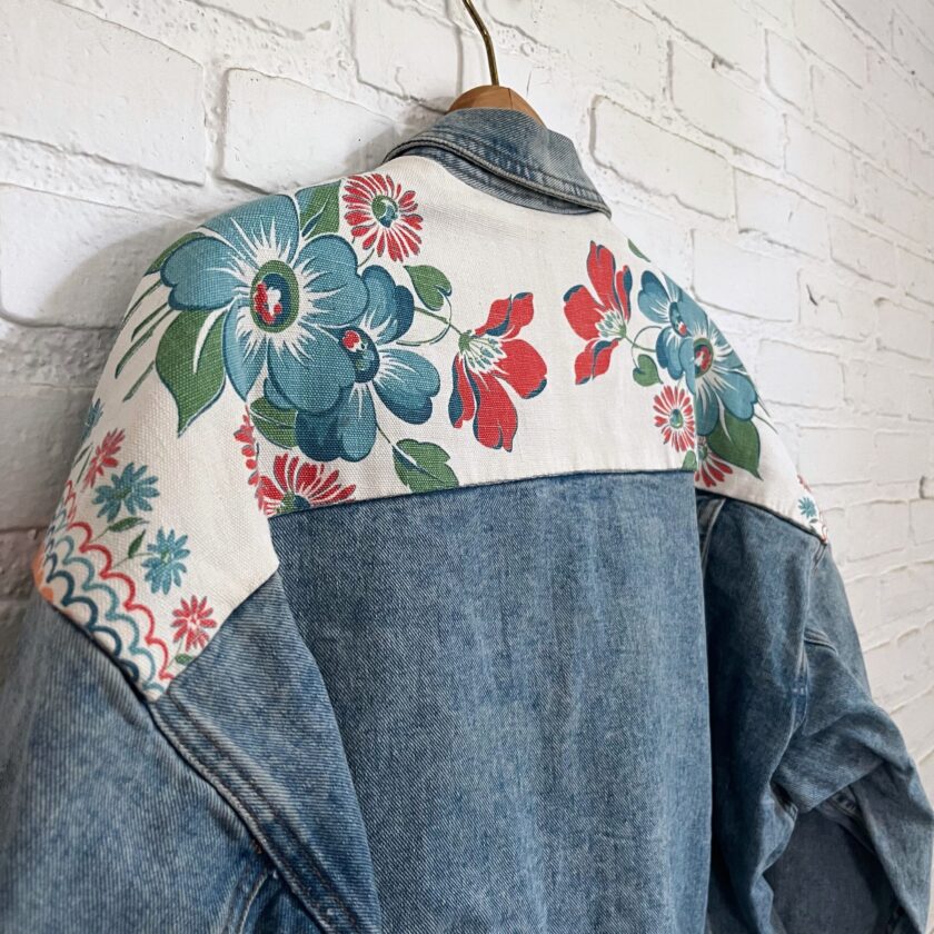 A denim jacket with flowers on it hanging on a brick wall.