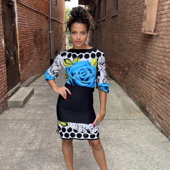 A woman in a blue and black dress posing in an alleyway.