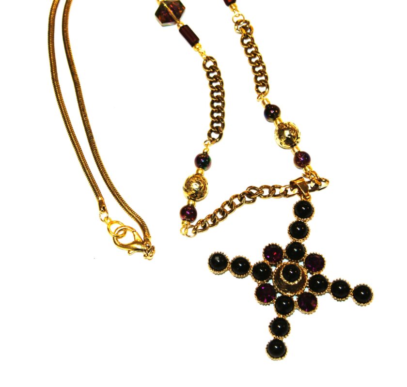 A gold tone necklace with a cross withy purple faceted stones and black beads