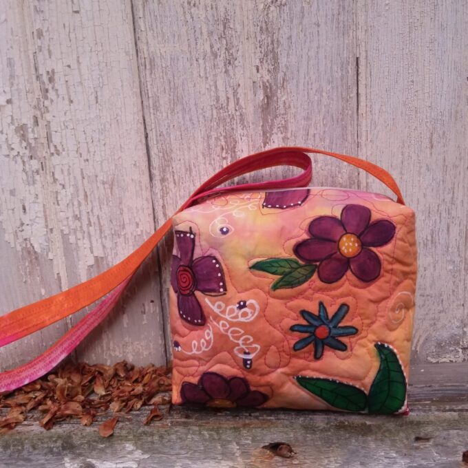 A unique, upcycled hand bag with painted flowers sitting on a shelf