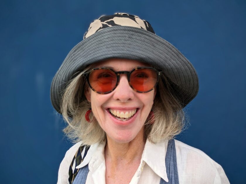 A woman wearing a hat and sunglasses smiles.