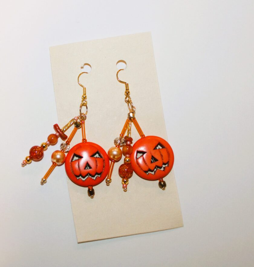 A pair of orange jack o lantern earrings hanging on a piece of paper.