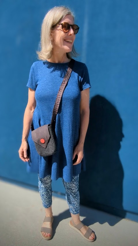 A woman wearing a blue t - shirt and sunglasses standing in front of a blue wall.