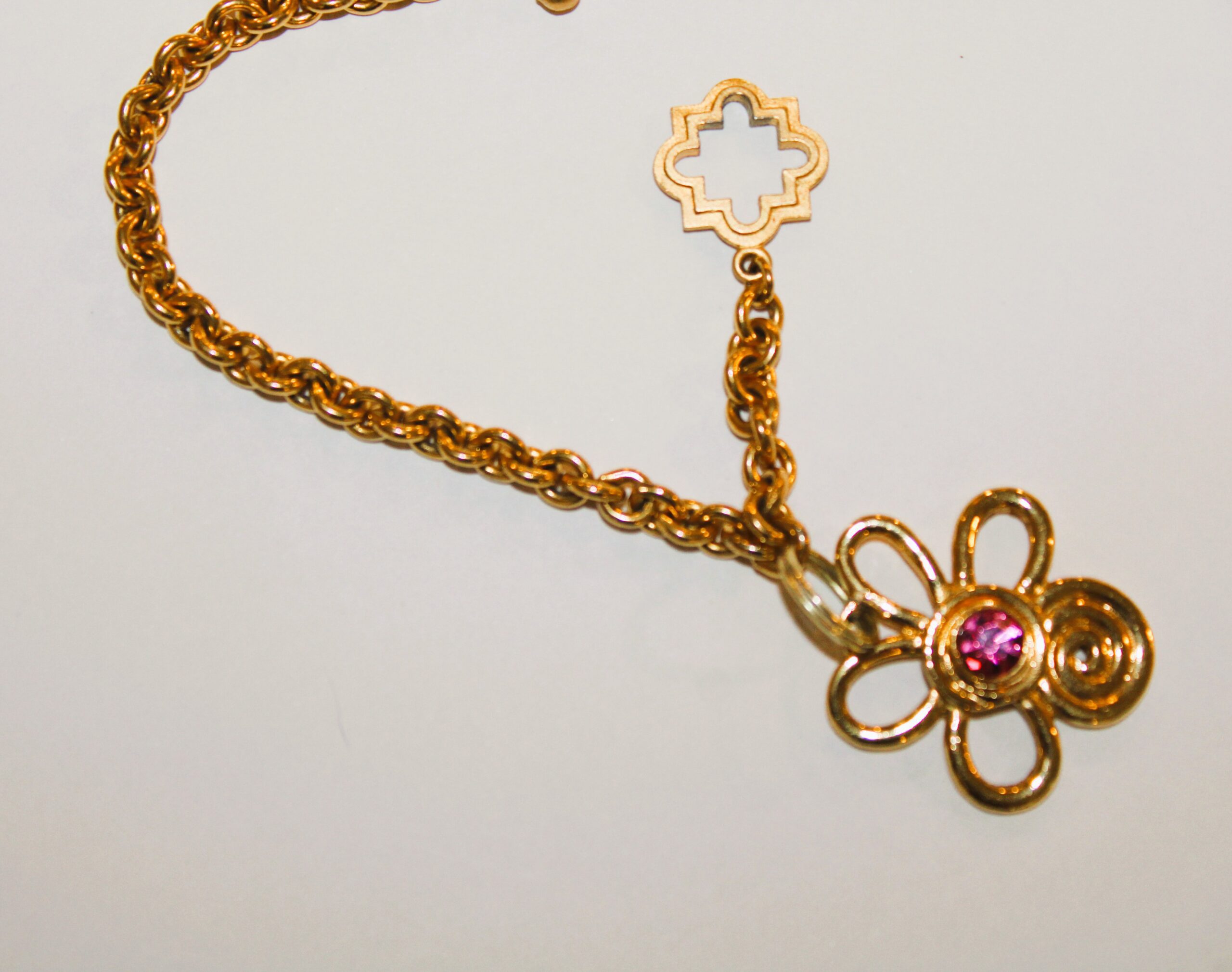 A gold chain with a pink stone in a flower charm.