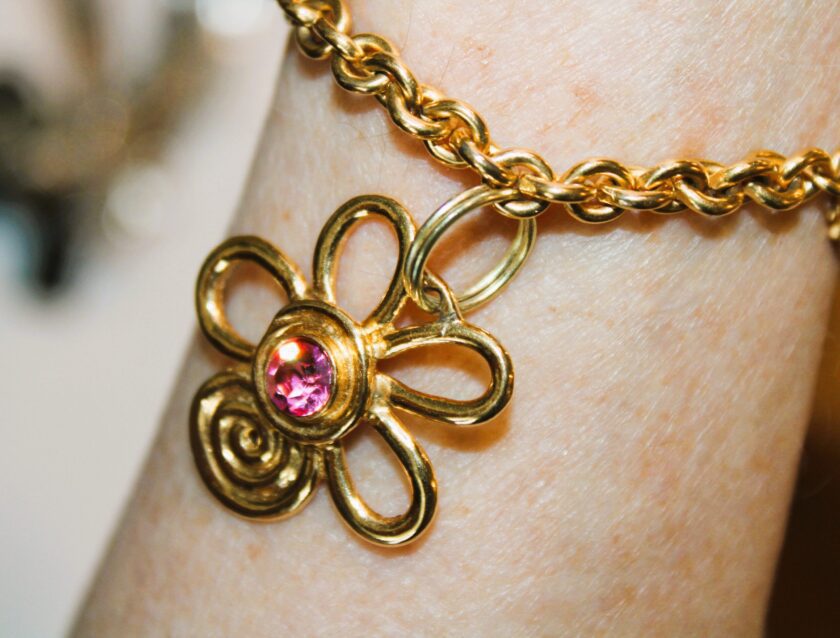 A gold bracelet with a pink flower on it.
