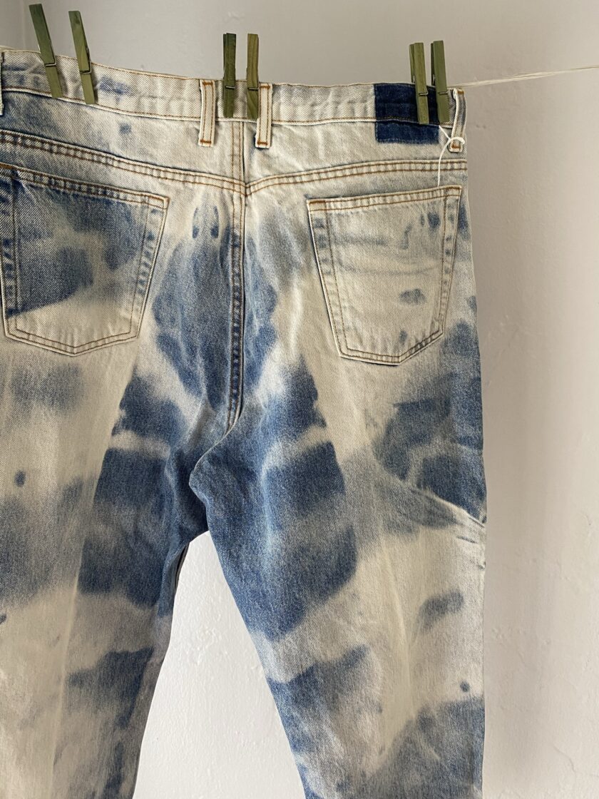 A pair of tie dyed jeans hanging on a clothes line.
